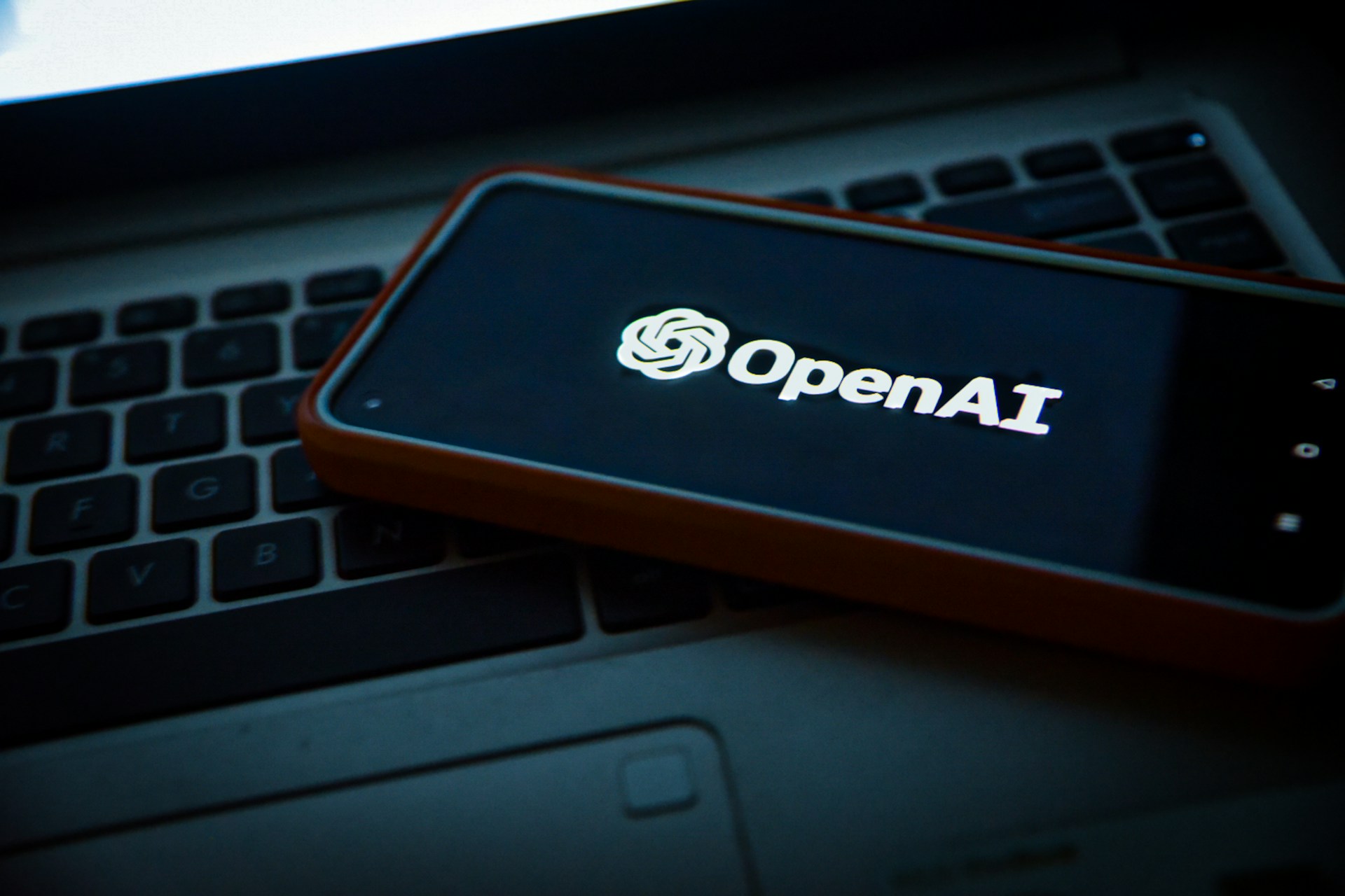 A smartphone displaying the OpenAI logo rests on a laptop keyboard.